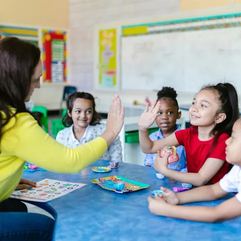Imagen de presentación de la FP Servicios Socioculturales y a la Comunidad en la que se ve una estudiante en una mesa ayudando y jugando con cuatro niñas de 5a 8 años.