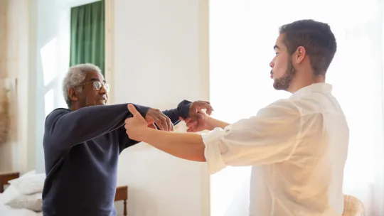 Hombre mayor en rehabilitación con su auxiliar de ayuda a domicilio.