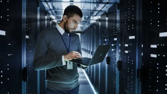 Informático en una sala de servidores, utiliza un portátil para configurar el sistema informático.