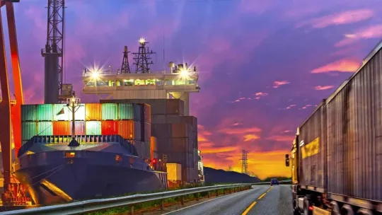 Puerto marítimo al lado de una carretera con transporte terrestre representan subsistemas logísticos.