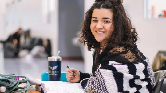 Estudiante joven sonriendo mientras escribe en su cuaderno