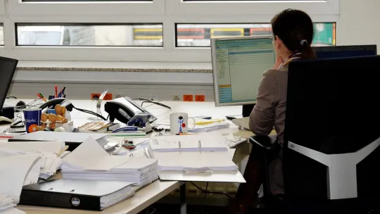 Trabajadora en su puesto de trabajo con muchos documentos.