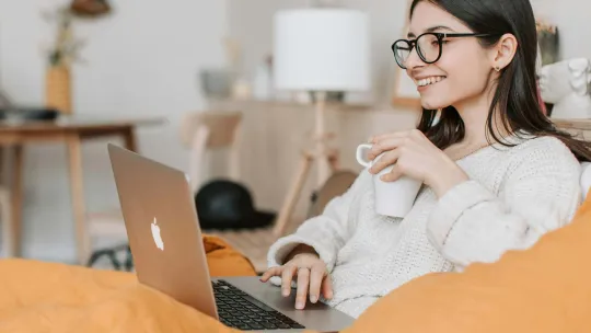 Chica en el sofá con un portátil, toma café y participa en clases online.