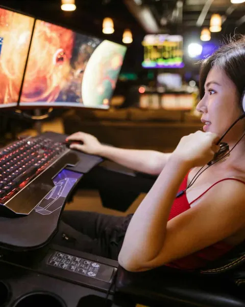 Una gamer, reclinada, juega a videojuegos en su ordenador con tres pantallas.
