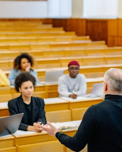 Alumnos sentados y escribiendo en cuadernos en clase mientras el profesor explica