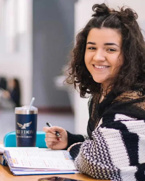 Estudiante joven sonriendo mientras escribe en su cuaderno