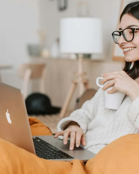 Chica en el sofá con un portátil, toma café y participa en clases online.